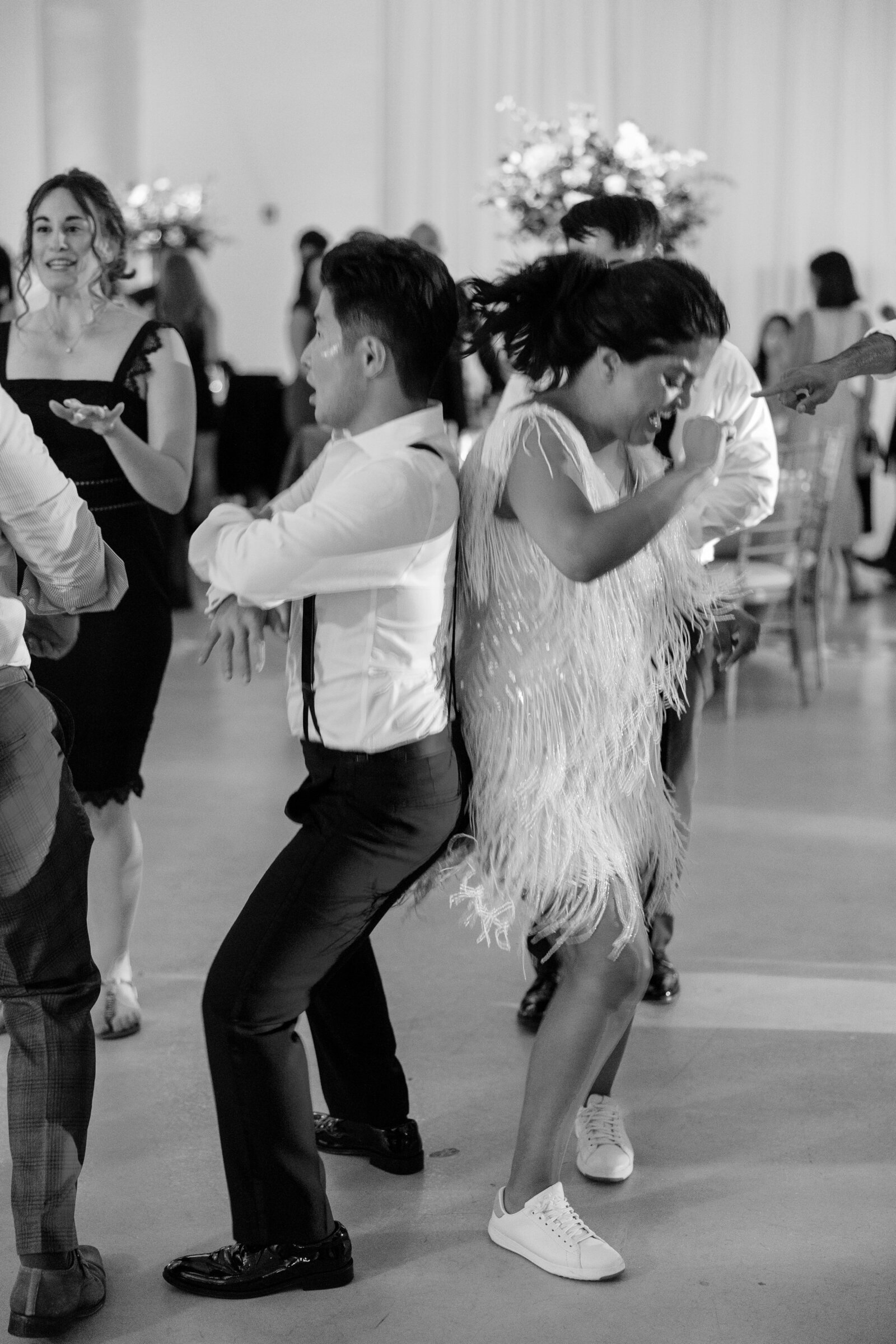 Black and white photo of guests dancing back to back on a crowded reception dance floor.